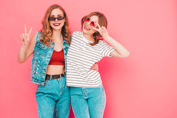 Two young beautiful smiling hipster female in trendy summer hipster  clothes. Sexy carefree women posing near pink wall in studio. Trendy and positive models having fun. Cheerful and happy - 写真・画像