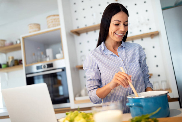 Happy beautiful woman in kitchen following recipe on digital device during cooking. - Fotoğraf, Görsel