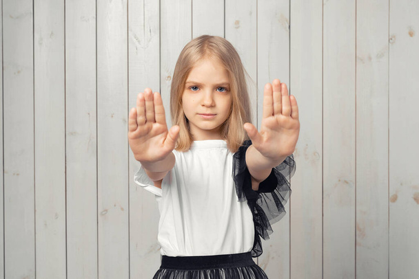 Říkám ne. Vážné blondýny dospívající dívka drží obě dlaně před kamerou, dělá zakázané znamení, omezuje nebo varuje, natahuje ruku v stopce. Studio záběr, světlé dřevěné pozadí - Fotografie, Obrázek