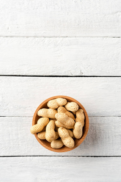 Tasty peanuts in bowl on white wooden background with copyspace. Top view - Фото, зображення