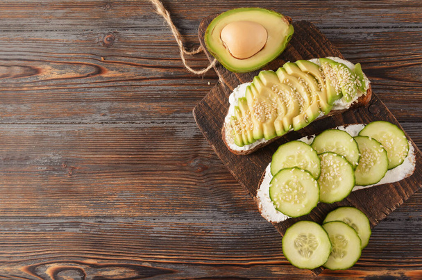 2 sandwiches with cucumber, soft cheese,  and avocado on a wooden background  - Foto, Imagem