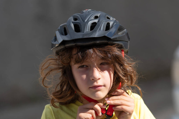portrait of little boy with long hair fastens his red safety helmet ready to ride a bike - Valokuva, kuva