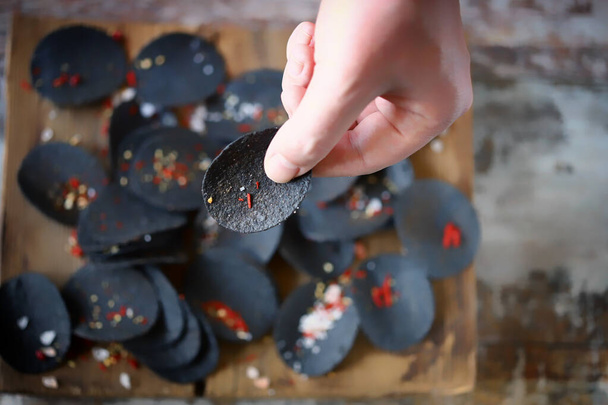 Black chips with spices in hand. Black food. - Photo, Image