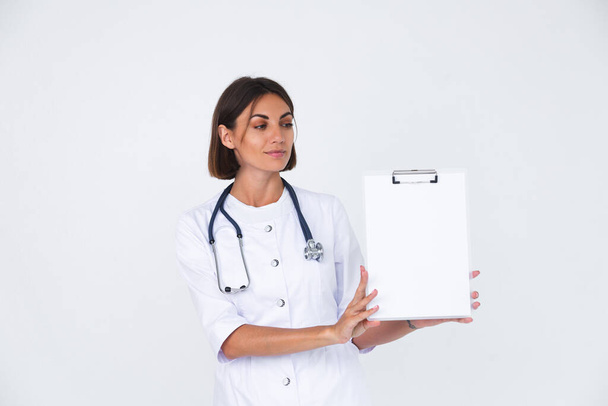 Женщина-врач в лабораторном халате на белом фоне изолирована, уверенная в себе улыбка удерживает белую бумагу пустой с пустым местом - Фото, изображение