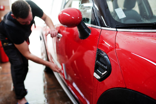 Man worker washing red car in detailing garage. - Foto, Bild
