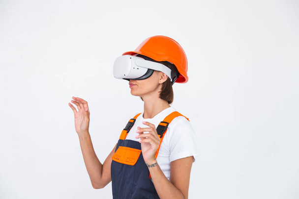 Hezká žena inženýr v budování ochranné přilby na bílém pozadí ve virtuální realitě brýle - Fotografie, Obrázek