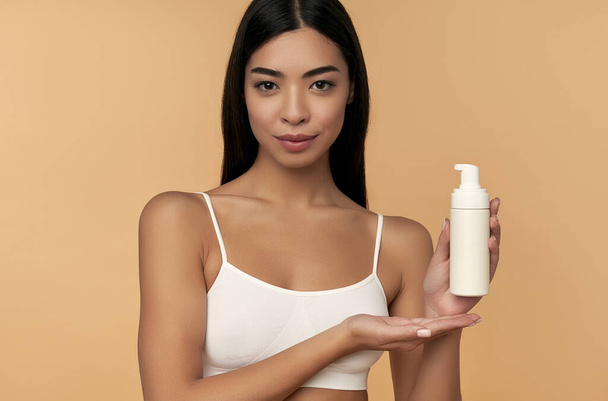 Jovem mulher asiática em lingerie branca com pele brilhante com garrafa de foa facial - Foto, Imagem