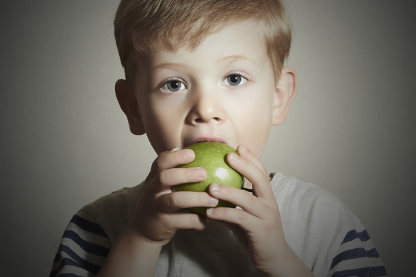 面白い子供はリンゴを食べる。緑のリンゴと小さなハンサムな男の子。健康食品。果物だ。食事を楽しむ - 写真・画像