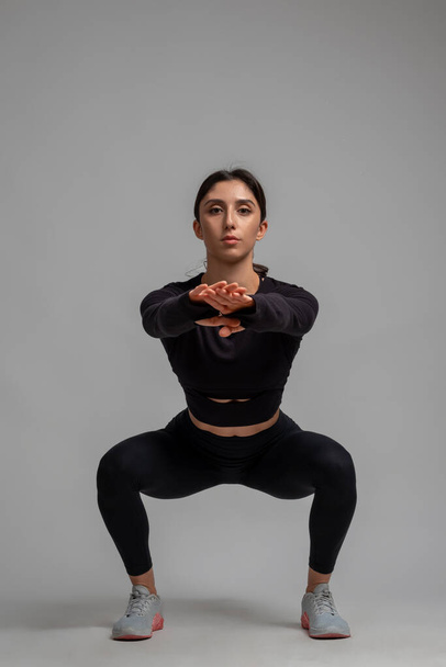 Jeune femme sportive faisant squats sur fond gris - Photo, image