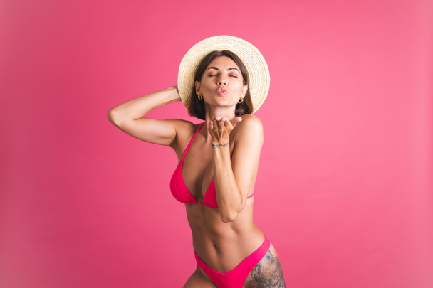 Beautiful fit tanned sporty woman in bikini and straw hat on pink background - Photo, Image