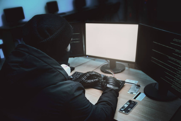 Shot from the Back to Hooded Hacker Breaking into Corporate Data Servers from His Underground Hideout. Place Has Dark Atmosphere, Multiple Displays - Photo, Image