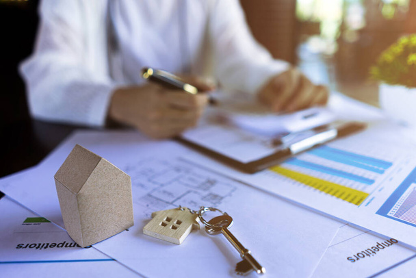 Профессиональные агенты по недвижимости рассчитывают цены на жилье с помощью ключей от дома, миниатюрных типовых домов, проектных документов. - Фото, изображение
