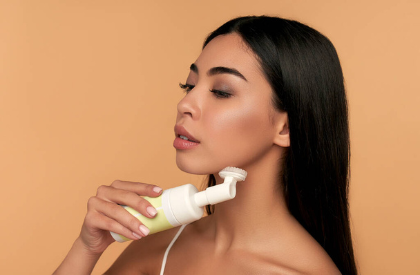 Young asian woman with radiant skin cleans her face with a brush and foa - Foto, Imagem