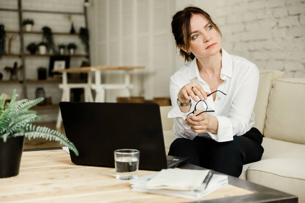 Middle aged business woman working at home using laptop, pensive looking away - Foto, Bild