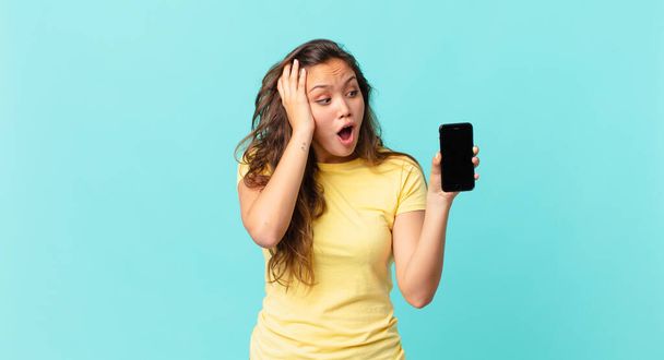 young pretty woman feeling happy, excited and surprised and holding a smart phone - Фото, зображення