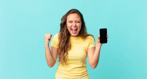 young pretty woman shouting aggressively with an angry expression and holding a smart phone - Foto, imagen