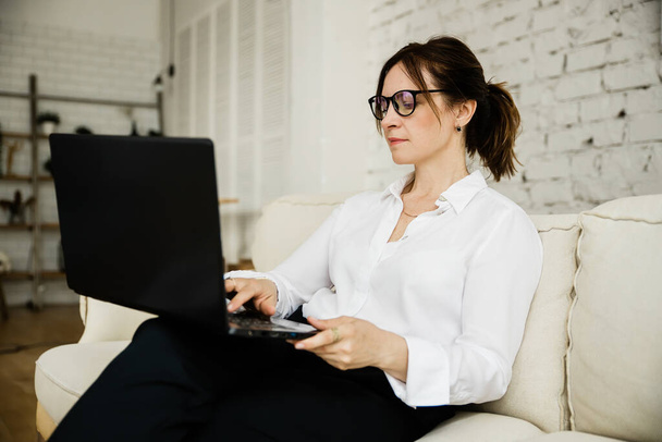 Middle aged business woman working at home using laptop, side view. - Фото, зображення