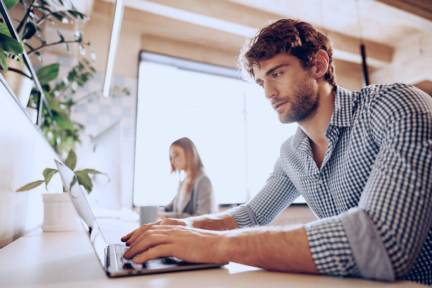 Young bearded successful businessman working on laptop in office with female colleague - Foto, Imagen
