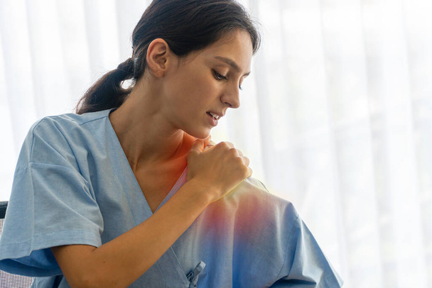 Insurance and health care sickness concept. Unhappy patient young woman holding hand on own pain shoulder or office syndrome or injury neck while sitting in the room at hospital. - Foto, imagen