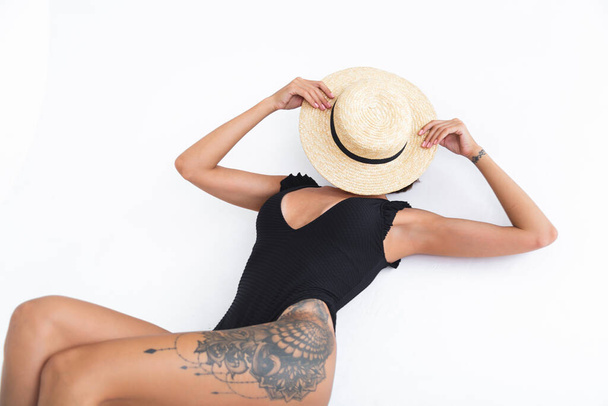 Fit tanned woman in black swimsuit and straw hat on white background posing - Φωτογραφία, εικόνα