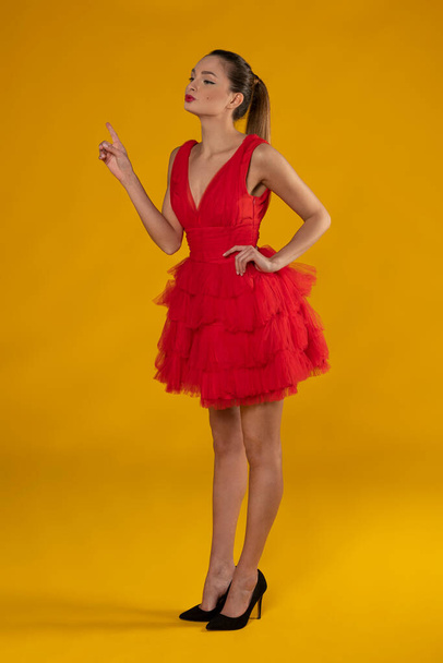 beautiful woman in red outfit , posing on yellow in pin-up style , she is looking on one side .in act to indicate - Foto, Imagen