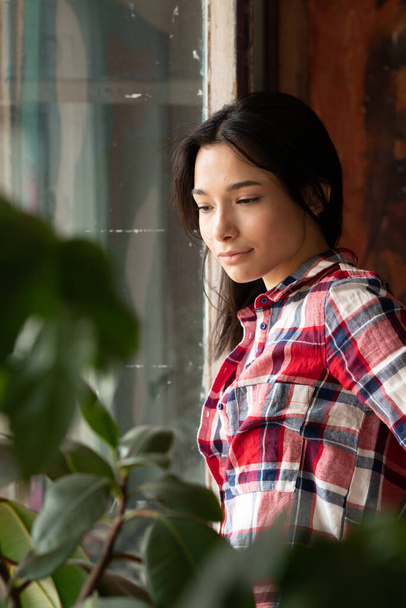 fiatal gyönyörű nő pózol a stúdióban, áll az ablak mellett egy kockás ing és farmer - Fotó, kép