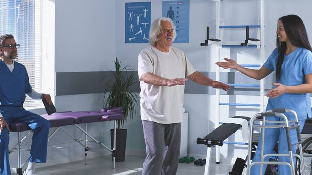 Rehabilitation therapists teaching elderly man to walk - Photo, Image