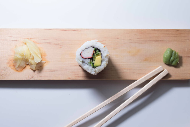 A top view of a California tempura roll on a narrow wooden board with wasabi and pickled ginger slices - Foto, afbeelding