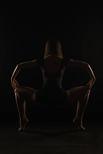 Bailarina está sosteniendo una bonita postura en cuclillas desde la espalda en la silueta - Foto, imagen