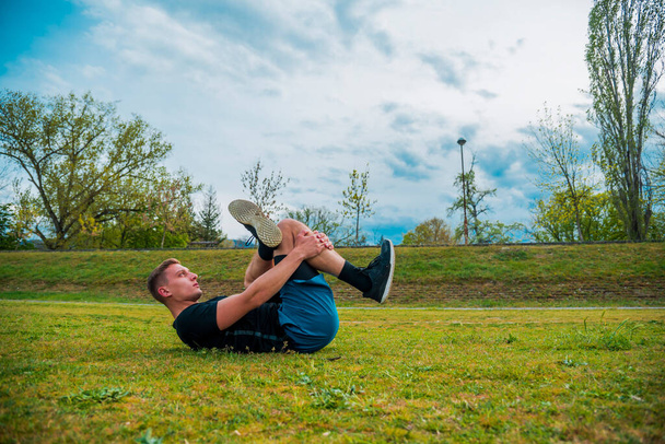 Sport e yoga. Un uomo con la barba, in abbigliamento sportivo esegue stretching sull'erba prima dell'allenamento - Foto, immagini