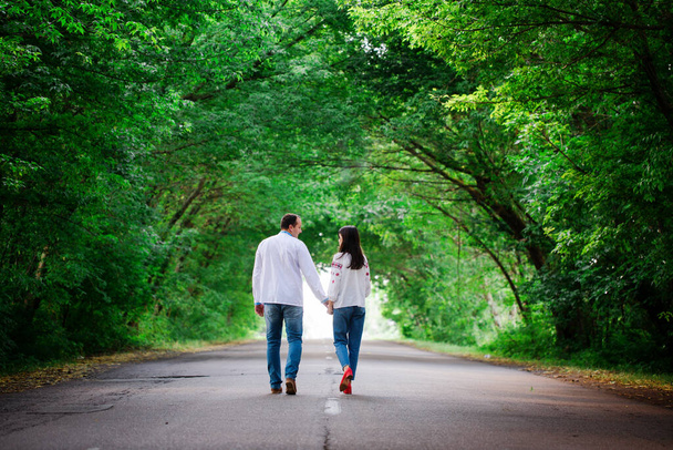 Un homme et une femme marchent le long de la route dans un tunnel d'arbres se tenant la main. Vue arrière - Photo, image