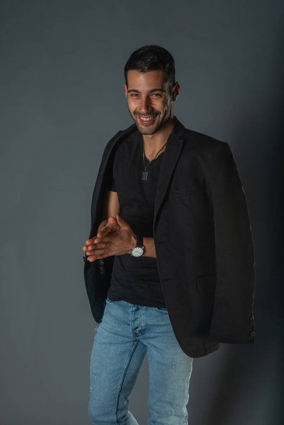 Handsome fashionable model in a black t-shirt with a jacket on his shoulders posing in a studio - Fotoğraf, Görsel