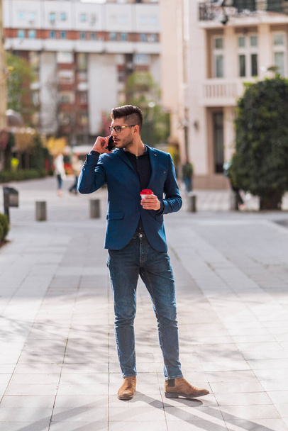 Uomo d'affari alla moda con caffè che cammina su città sqaure mentre parla su telefonino - Foto, immagini