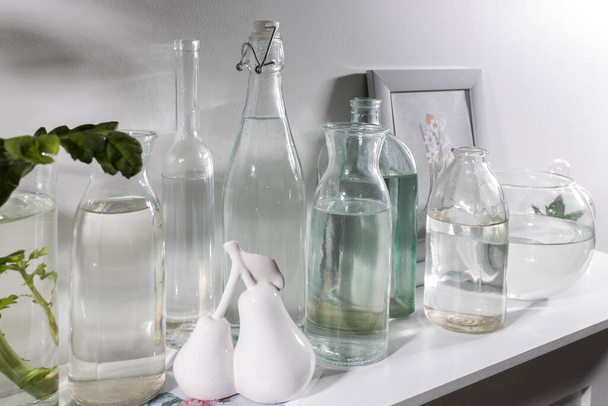 A set of bottles of different shapes with water with a photo frame is on the chest of drawers. Copy space - Foto, Imagem