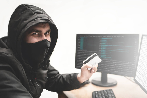 Cunning hacker fraudster in white background with stolen credit card in hand tries to steal money from bank account. Internet theft concept - Foto, Imagen