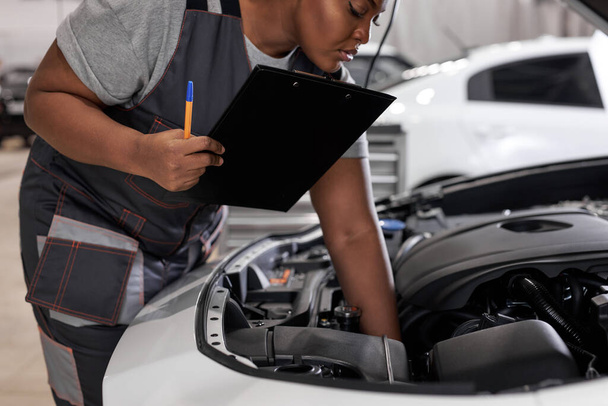 african Female mechanic at work, checking car hood writing notes in tablet - Foto, immagini