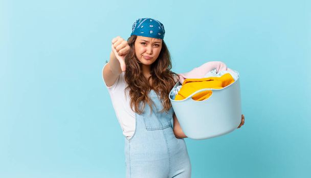 young pretty woman feeling cross,showing thumbs down and holding a wash clothes basket - Photo, image
