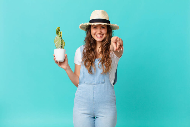 young pretty woman pointing at camera choosing you and holding a cactus - Фото, изображение