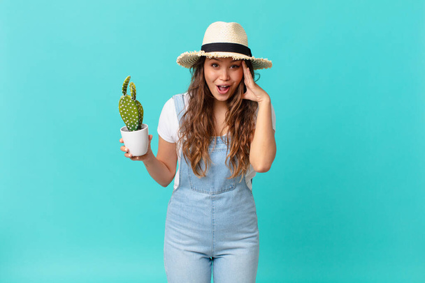 young pretty woman looking happy, astonished and surprised and holding a cactus - Fotoğraf, Görsel