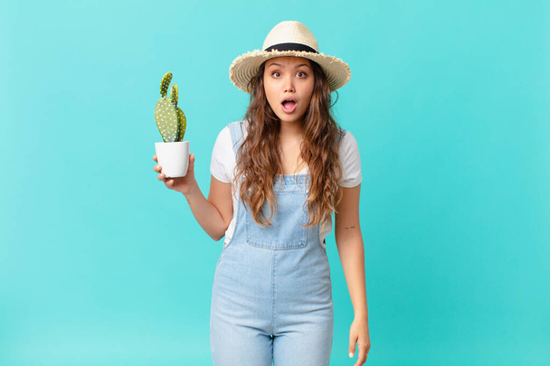 young pretty woman looking very shocked or surprised and holding a cactus - Zdjęcie, obraz