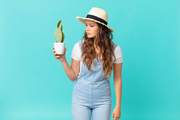 young pretty woman on profile view thinking, imagining or daydreaming and holding a cactus - Foto, Bild