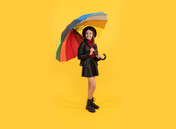 gelukkig stijlvol meisje in lederen kleding. Vrolijke tiener kind houden kleurrijke parasol. Een kind met een regenboogparaplu. Herfstseizoen. regenachtige weersvoorspelling. terug naar school. valmode accessoire. - Foto, afbeelding