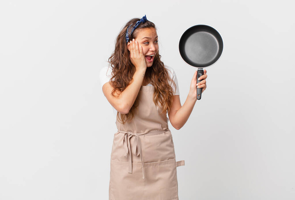 young pretty woman feeling happy, excited and surprised chef concept and holding a pan - Foto, Bild