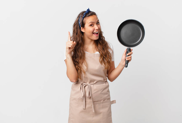 young pretty woman feeling like a happy and excited genius after realizing an idea chef concept and holding a pan - Foto, immagini