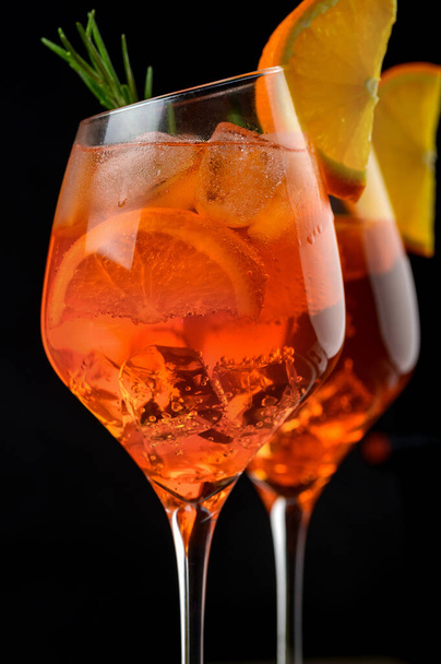 Ein eiskalter Aperol Spritz Cocktail wird in einem Weinglas serviert, das mit Orangen- und Rosmarinzweigen dekoriert ist. Schwarzer Hintergrund. Kopierraum - Foto, Bild