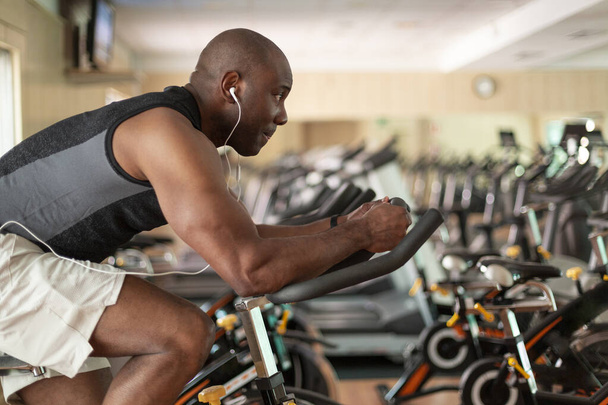 Athletic black man doing cardio workout on exercise bike in gym. Concept of sport and healthy lifestyle. - Фото, зображення