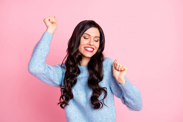 Photo of funny girl close eyes raise fists toothy beaming smile wear blue pullover isolated pink color background - Fotografie, Obrázek