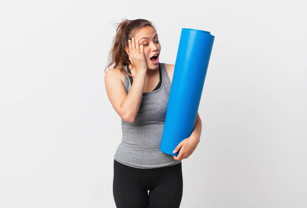 young pretty woman feeling happy, excited and surprised and holding a yoga mat - Photo, image