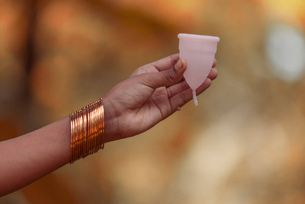 Yeniden kullanılabilir silikon regl kupası tutan Hintli genç bir kız. Açık hava görüntüsü. - Fotoğraf, Görsel
