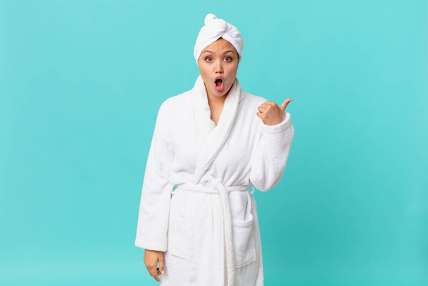 young pretty woman looking astonished in disbelief and wearing bath robe after shower - 写真・画像